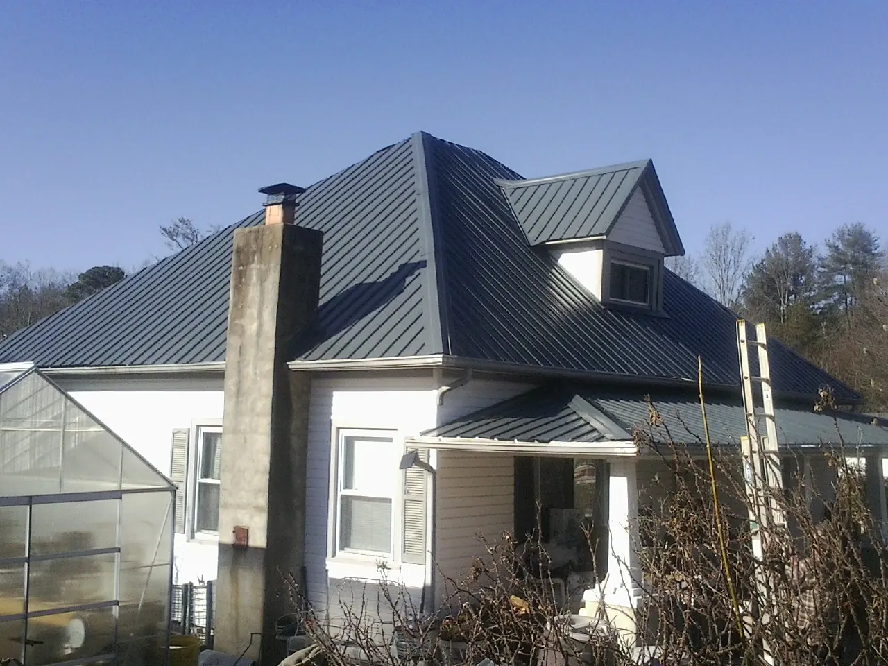 Dark blue standing seam metal roof on a white farmhouse with dormer — Slate & Tile Roof Repair by Roofing Brothers in Appleton