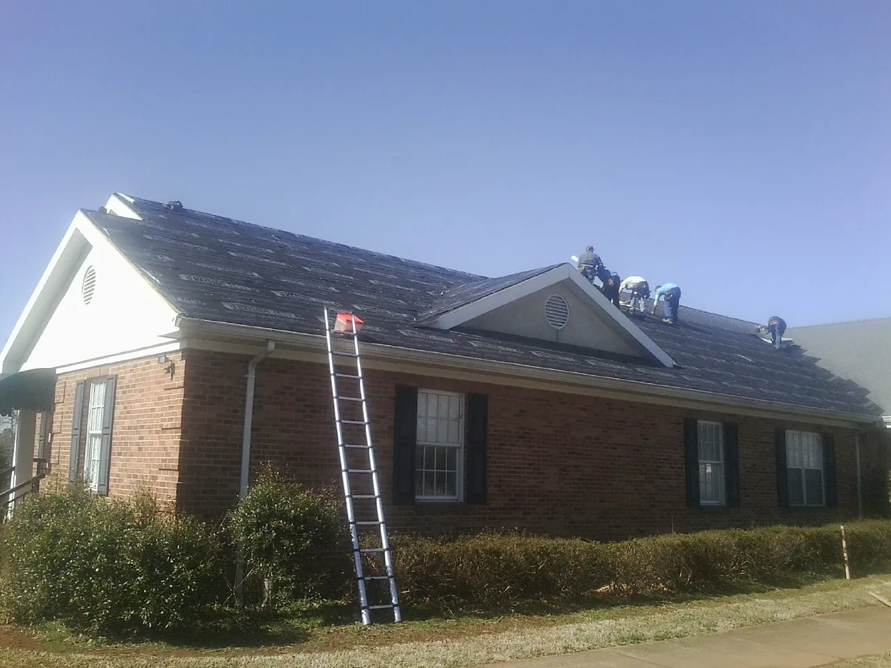 Crew tearing shingles off a brick ranch roof with a ladder set — Metal Roof Repair work by our crew in Appleton