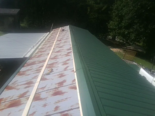 Old rusted panels beside newly installed green metal roofing — Wind Damage Roof Repair by Roofing Brothers in Appleton