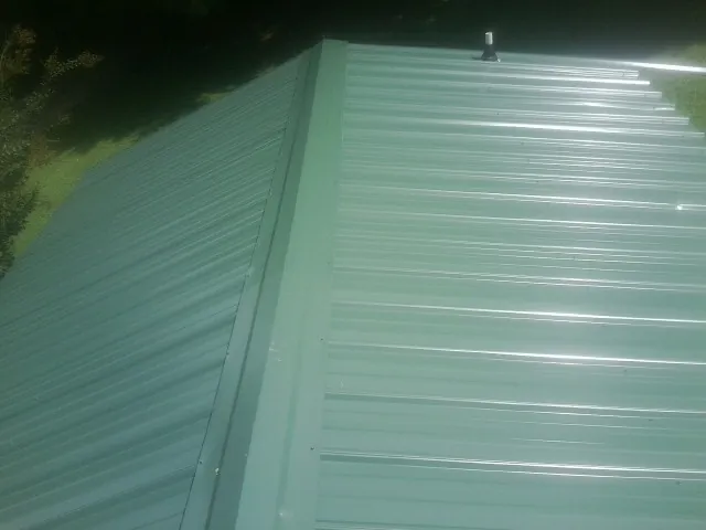 New green metal panels meeting at the ridge of a roof — Flat Roof Repair work by our crew in Appleton
