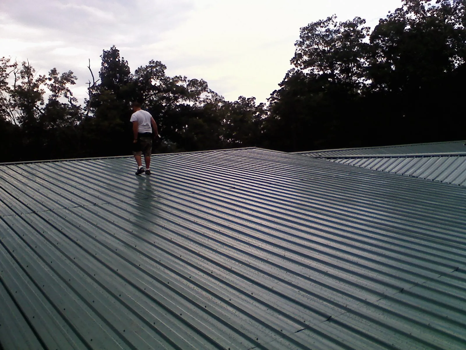 Roofer walking a wide expanse of new green metal roofing in Appleton